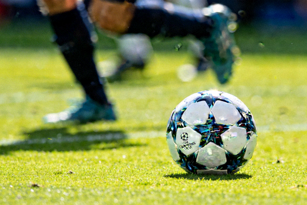 欧冠比赛用球在绿茵场上的特写，背景是模糊的球员身影